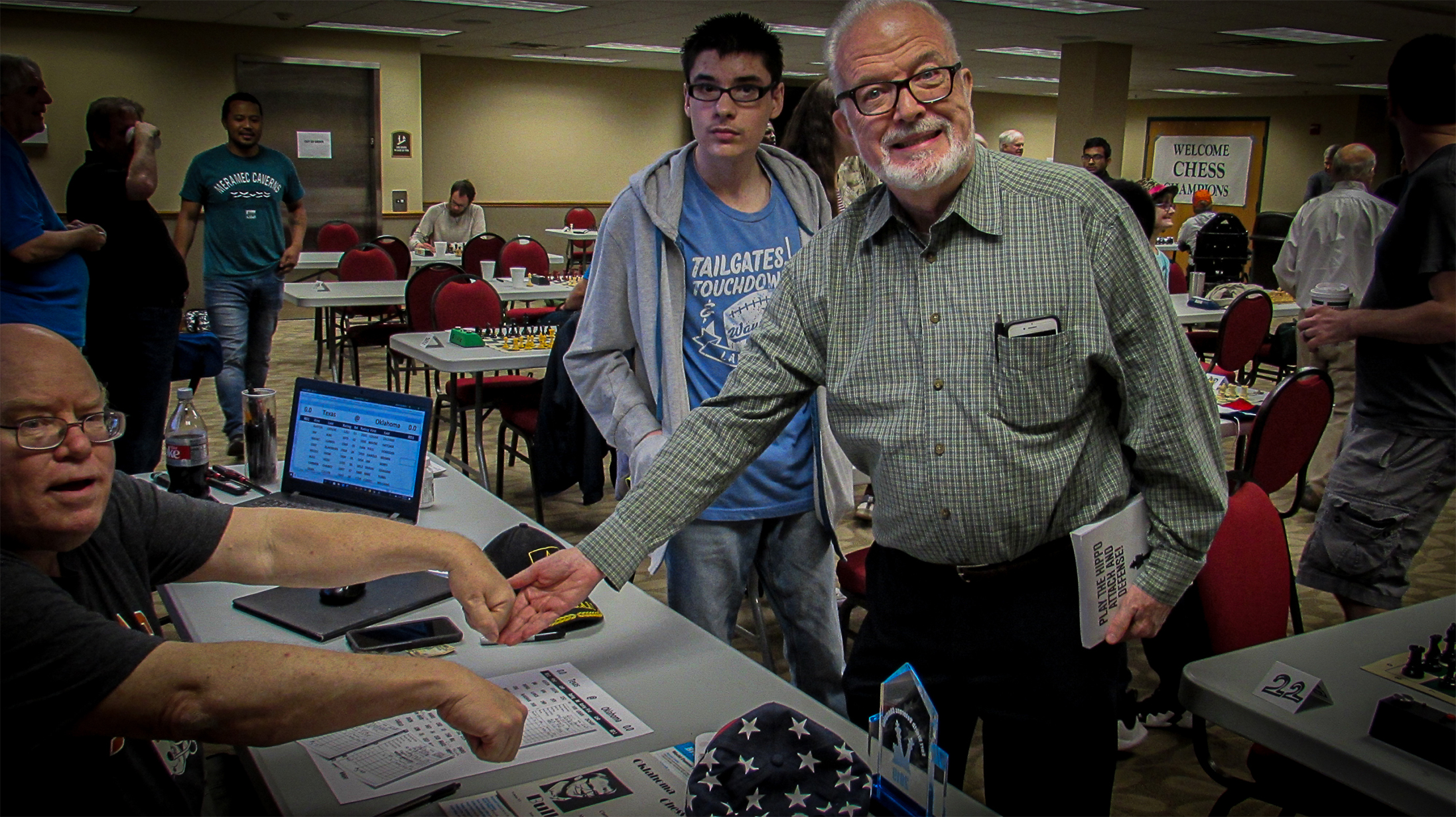 In accordance with tradition, Chief TD Jim Hollingsworth (left) extends both hands with a different colored pawn in each.  As the highest ranked player in the Murray County Open, Roy Cram (right) has the honor of drawing for colors while Jayden Dewbre (middle) looks on.  Photo by Mike Tubbs.